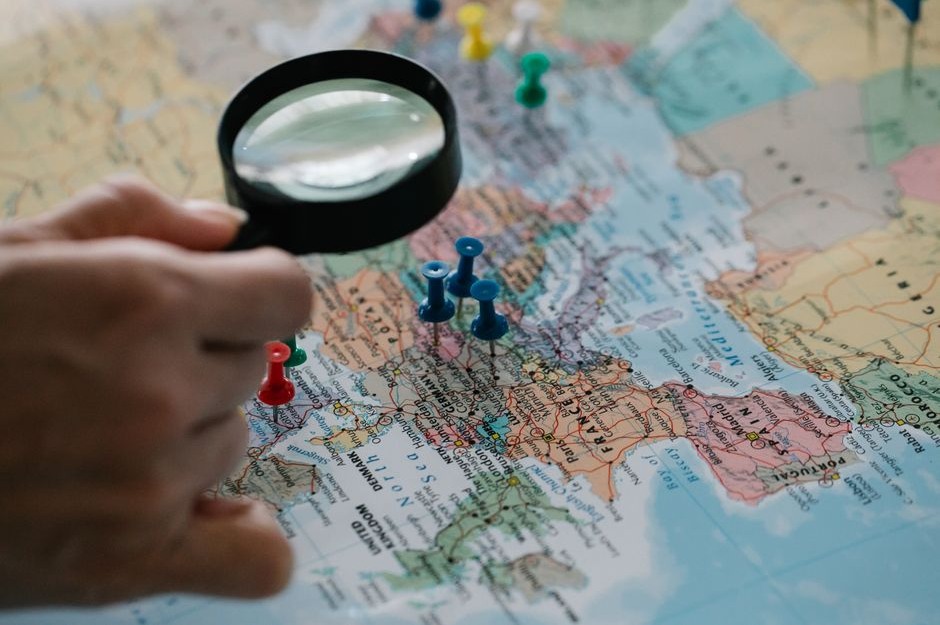 A hand holding a magnifying glass over a detailed paper map.