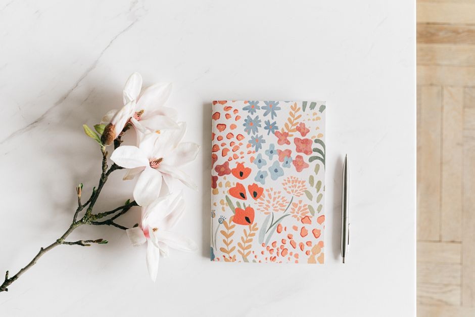 Floral notebook and blossom arranged on a light tabletop.